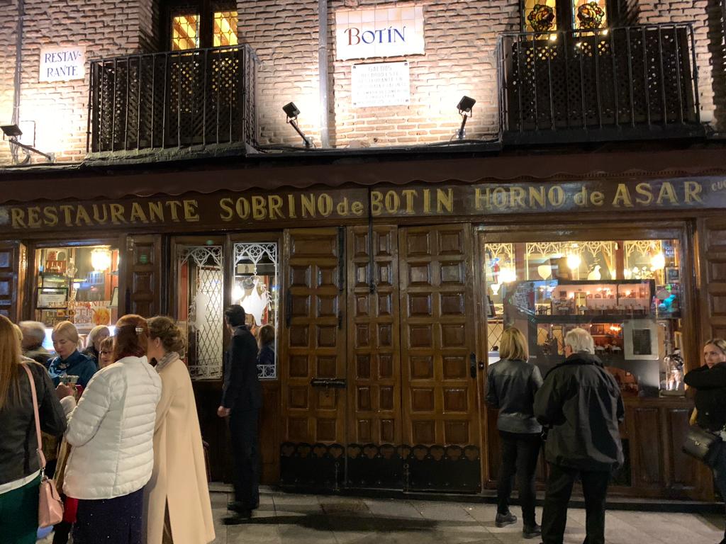 Fachada de madeira escura iluminada do restaurante Sobrino de Botín em Madri à noite com clientes e turistas na calçada.