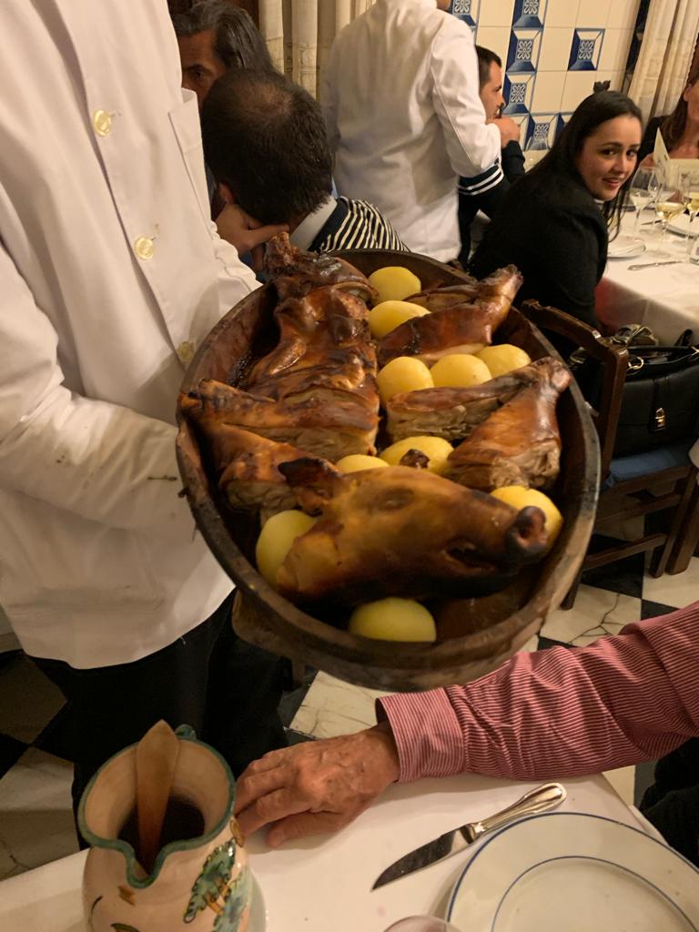 Garçom de jaleco branco servindo um leitão assado inteiro com batatas cozidas em uma travessa oval de barro no restaurante Botín em Madri.