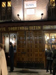 Fachada de madeira escura iluminada do restaurante Sobrino de Botín em Madri à noite com clientes e turistas na calçada.