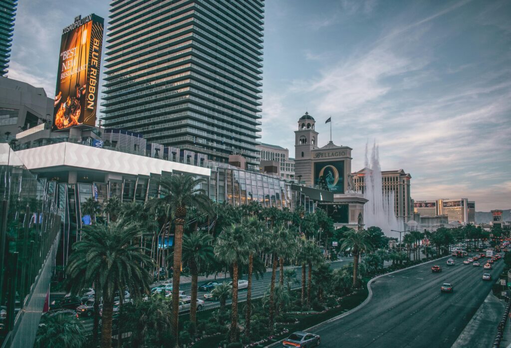 Vista aérea da avenida Strip em Las Vegas, com coqueiros no canteiro central, carros circulando e o show das fontes do Hotel Bellagio ao fundo.