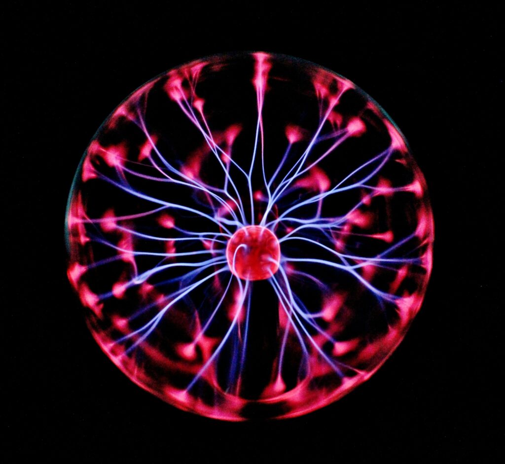 Uma lâmpada ou globo de plasma aceso exibindo raios elétricos azuis e ramificações rosa-choque contra um fundo preto.