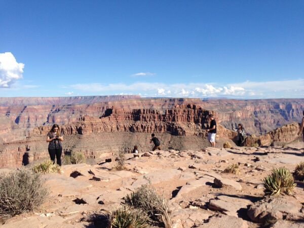 Turistas espalhados por um mirante de rocha natural observando as imensas formações rochosas esculpidas do Grand Canyon, nos Estados Unidos.