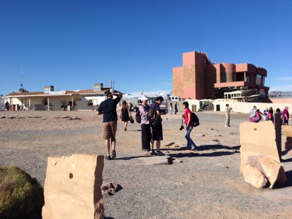 Visitantes caminhando pela área externa do Grand Canyon Skywalk, no Arizona, Estados Unidos, com edifícios de apoio e o Skywalk Cafe ao fundo sob céu azul.