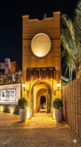 Fachada noturna iluminada do Restaurante Porto Porto em Florianópolis, destacando a entrada em arco de estilo rústico e um painel de azulejos com o nome do estabelecimento ao lado esquerdo.