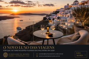 Mesa posta para duas pessoas em uma varanda luxuosa em Santorini, na Grécia, com taças de vinho e vista para o mar e construções brancas durante o pôr do sol. Abaixo, banner preto com o texto "O novo luxo das viagens: por que os turistas estão fugindo das multidões em 2026?"